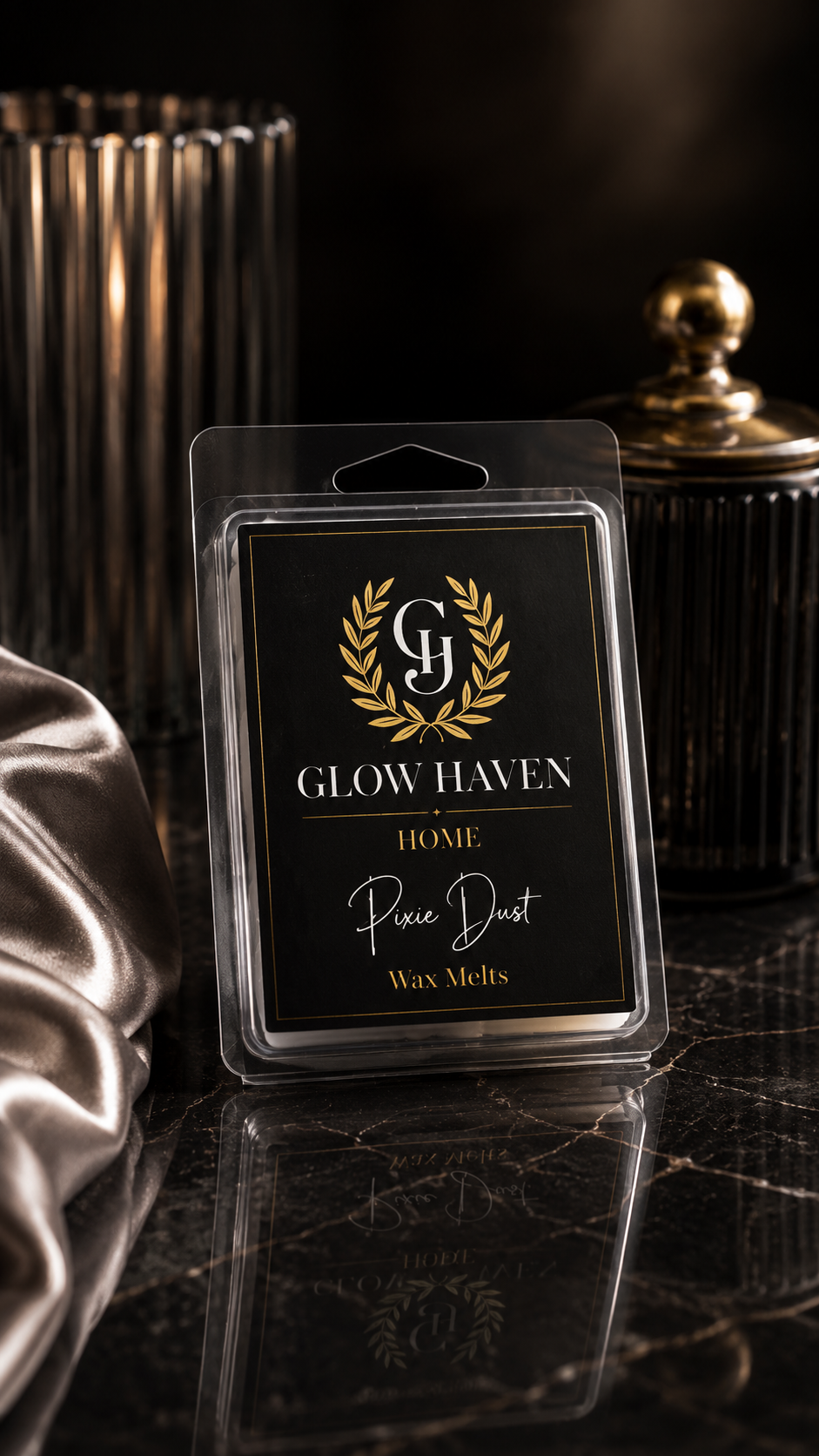 Glow Haven Pixie Dust clam shell wax melt in a black and gold labelled pack beside silver satin